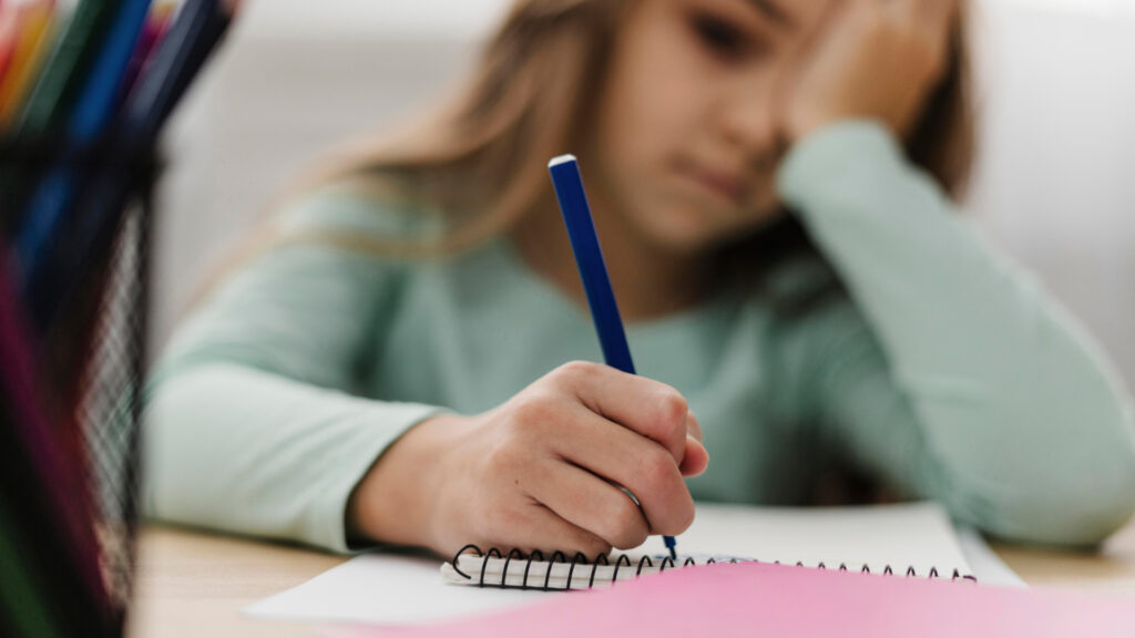 Una bambina dall'espressione stanca e triste che fa i compiti