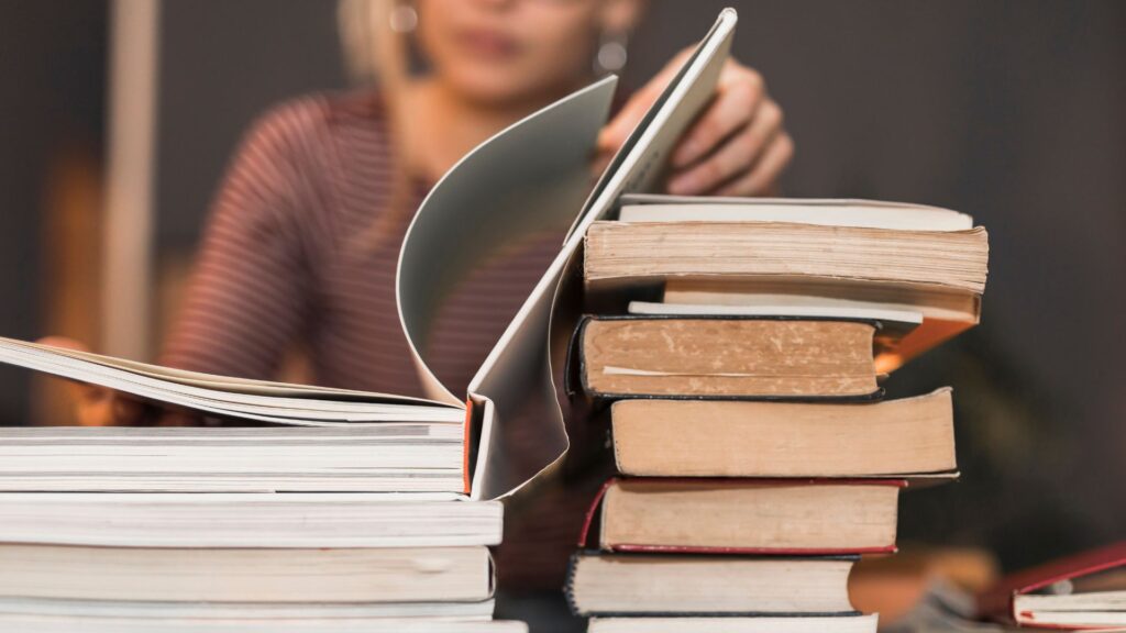 Ragazza con grossa pila di libri da studiare davanti a sé