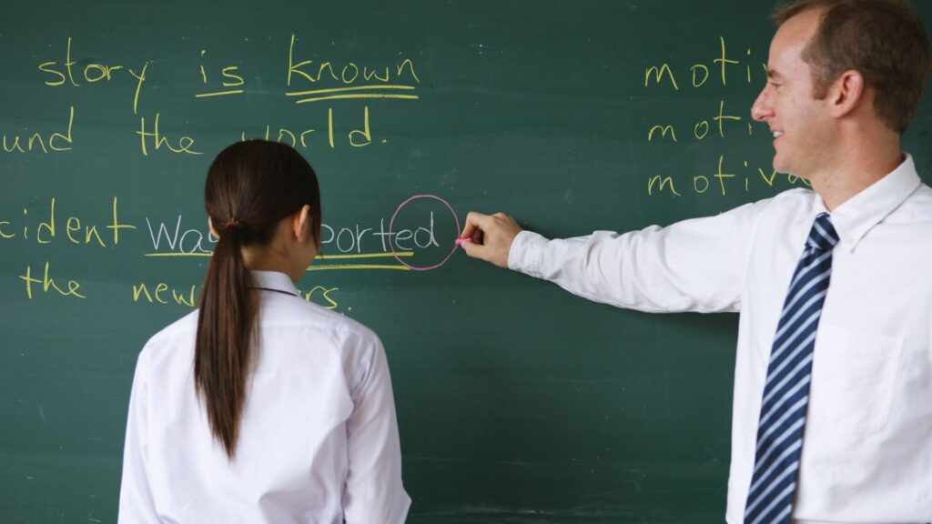 Studentessa alla lavagna viene corretta dall'insegnante di inglese